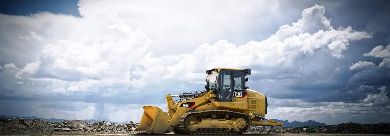 Yellow track loader on open ground under a wide sky