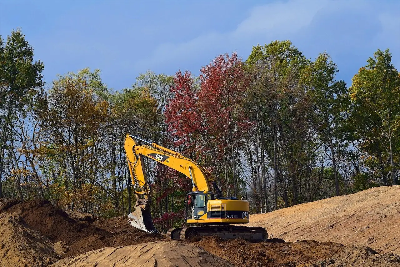 Yellow excavator digging in sandy soil with trees behind